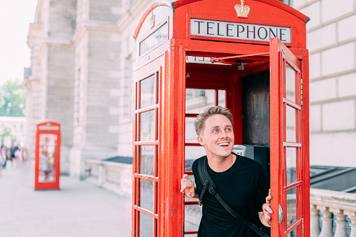 Portrait of a Cheerful Young Man Looking Out From an Iconic Red Telephone Booth in London, United Kingdom