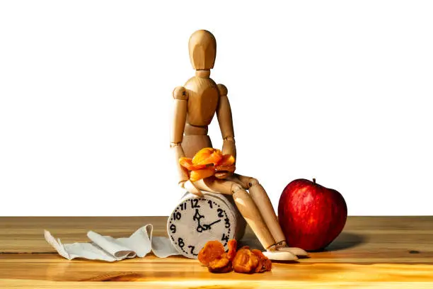 Photo of Wooden figure sit on a roll of toilet paper near alarm clock and apples. Concept of the problem with digestion.