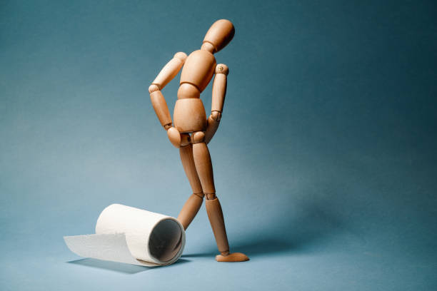 Wooden figure standing next to roll of toilet paper. Concept of the problem with digestion. stock photo