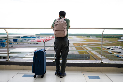 A  male tourist with luggage trolley waiting for his flight at the airport