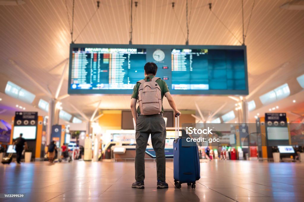 Male tourist looking at arrival and departure board at Kuala Lumpur International Airport Asian male traveler with wheeled luggage checking for flight schedule on arrival and departure board at Kuala Lumpur International Airport Travel Stock Photo