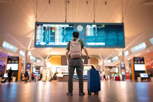 Male tourist looking at arrival and departure board at Kuala Lumpur International Airport Asian male traveler with wheeled luggage checking for flight schedule on arrival and departure board at Kuala Lumpur International Airport wheeled luggage stock pictures, royalty-free photos & images