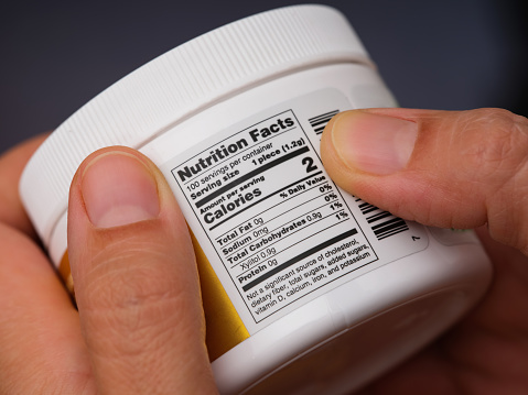 A woman holding a jar with gums and reading a Nutrition Facts label at the back.