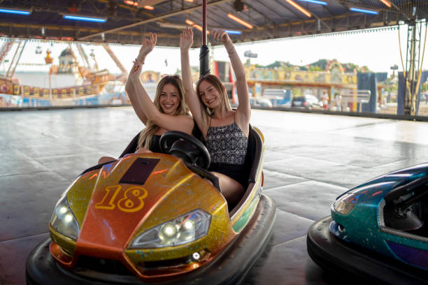istock Two young girlfriends are laughing and shouting while riding a bumper car at amusement park 1413301886