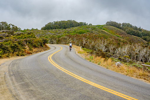 Curving asphalt road with yellow lines, and silhouette of the bicyclist, serpentine way.  Montana De Oro State Park, California, USA- July 13, 2022