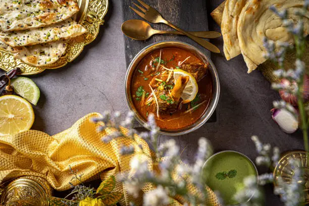 Photo of Nihari Gosht with paratha, chutney, raita, and roti served in a dish isolated on dark background top view food