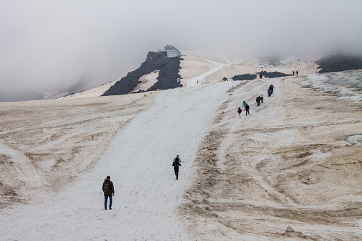 Tourists climb the snowy road to Elbrus among the fog and cloudy sky in the northern Caucasus in Kabardino-Balkaria russia