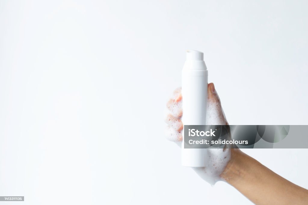 Facial Cleansing Foam Woman holding white plastic bottle against white background. Copy space for your design. Facial Cleanser Stock Photo
