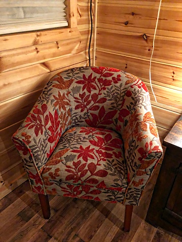 A cushioned chair covered with flowered upholstery in a wooden cabin