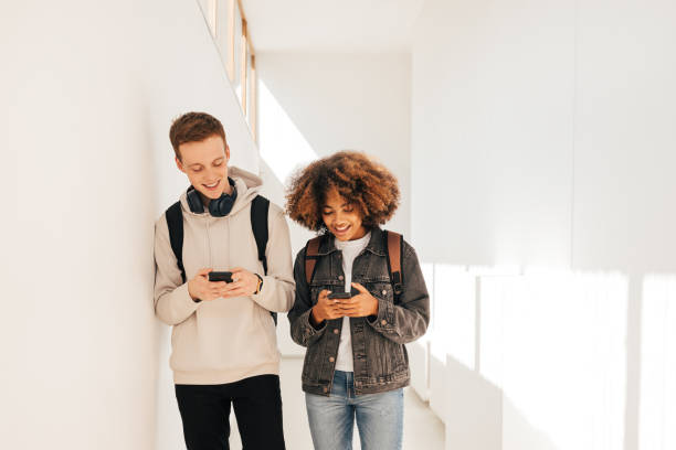 istock Laughing classmates walking together in corridor holds smartphones 1413317064