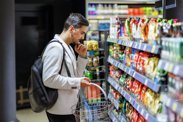 Not sure which type of coffee to buy A young Caucasian businessman is standing in a supermarket aisle and thinking about which coffee to purchase. ready to eat stock pictures, royalty-free photos & images