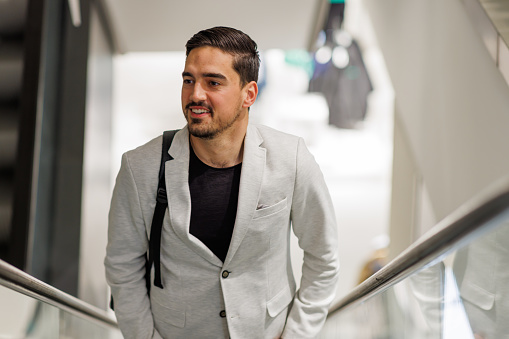 A young Caucasian businessman wearing a modern jacket is going up a flight of stairs with a smile on his face.