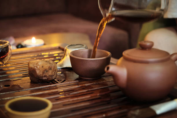 Brewing puerh tea. Traditional chinese tea ceremony. Tea pouring from teapot to glass cup on a tea tray. Moody low key selective focus