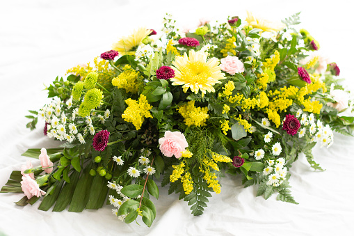 Funeral spray of yellow cremones, pink pixie carnations, kermit poms, maroon chrysanthemums, solidaster, white daisies, and ferns