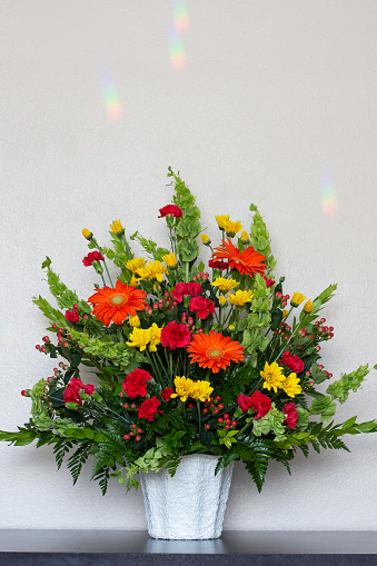 Funeral floral arrangement of orange and yellow daisies, red carnations, and red coffee bean