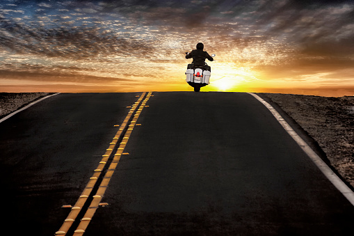 Image of a motorcycle traveling on a black asphalt highway into the sunset