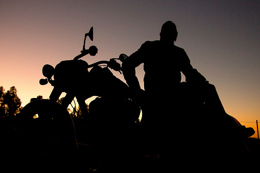 Silhouette of a man sitting on a motorcycle at sunrise or sunset