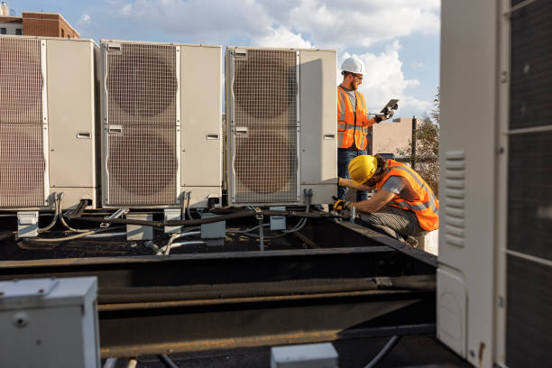 Team works together to inspect an air conditioner on a rooftop. Two construction workers are checking air condition system and logging results with a portable computer. stock photo