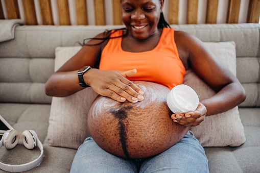 Pregnant woman applying skincare cream on her belly to prevent stretch mark