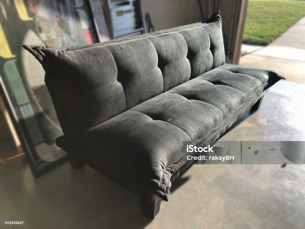 Black foldable futon bed set out in a garage Futon Stock Photo
