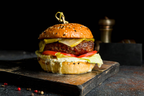 istock Burger with meat patty, vegetables and salted cucumbers on dark board 1413334640