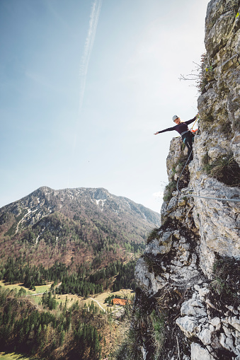 Woman climbing via ferrata trail in Slovenia, Europe on a beautiful sunny day in the spring. Woman mountaineer climbing on rocks, secured on a metal wire, while climbing up.
