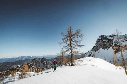 One lonely woman mountaineer hiking up the snowy mountain on a sunny winter day. Winter mountains covered in snow. Cold temperatures.