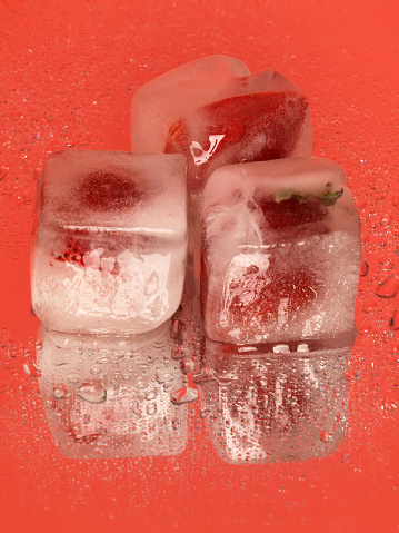 Strawberry ice cubes are isolated on a reflective background.