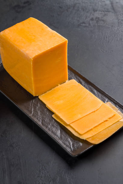 istock cheddar cheese sliced on black plate on dark table, vertical 1413336573