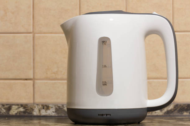istock Electric kettle. White plastic electric kettle on the kitchen table against the background of beige tiles on the wall. Kitchen equipment. Boiling water for tea, coffee, hot drinks. Copy space for text 1413341400