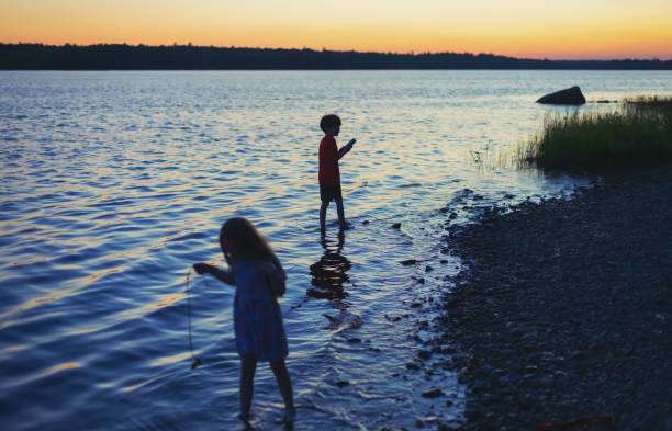 Brother & sister enjoy walking along a lake at dusk.