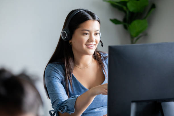 istock Young woman working in call center takes calls on headset while looking at computer screen 1413356801
