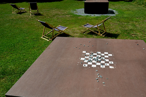 Park furniture chess table and chairs for four persons made of light metal and wooden beams with backrest on the bright glade area