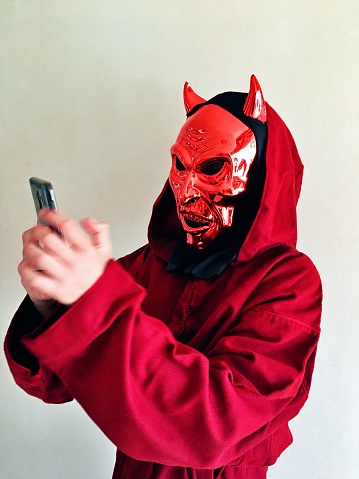 An unrecognisable person dressed up in a devil suit takes a selfie on their mobile phone.