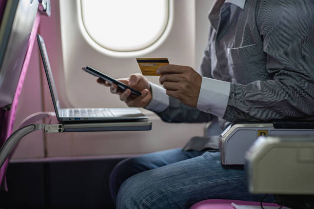 joven empresario con un teléfono inteligente y una tarjeta de crédito en línea trabajando en una computadora portátil sentada en un avión - easy money audio fotografías e imágenes de stock