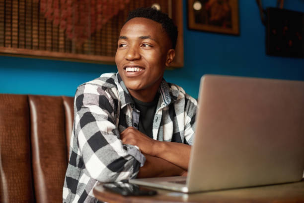 istock Stylish, trendy and thinking black male entrepreneur doing remote work in a vibrant restaurant. Happy young African man in deep thought sitting in a cafe or coffee shop and working 1413362413