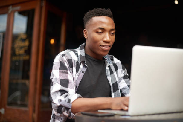 istock IT developer or freelancer working remotely and typing on laptop, sitting at an outdoor table of street cafe or restaurant. African American male student doing online learning, completing homework. 1413362464