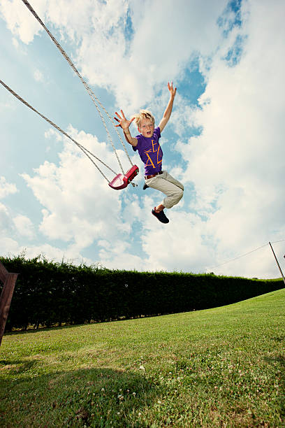 garçon sauter sur swing dans le jardin - bras en lair photos et images de collection