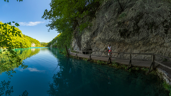 Young female tourist walks along a walkway running along an emerald lake in beautiful Plitvice