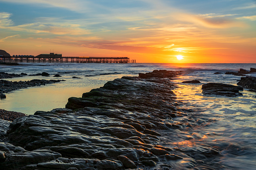The sun rising and the tide receding revealing the rocks on St Leonards beach with Hastings pier on the horizon, east Sussex south east England