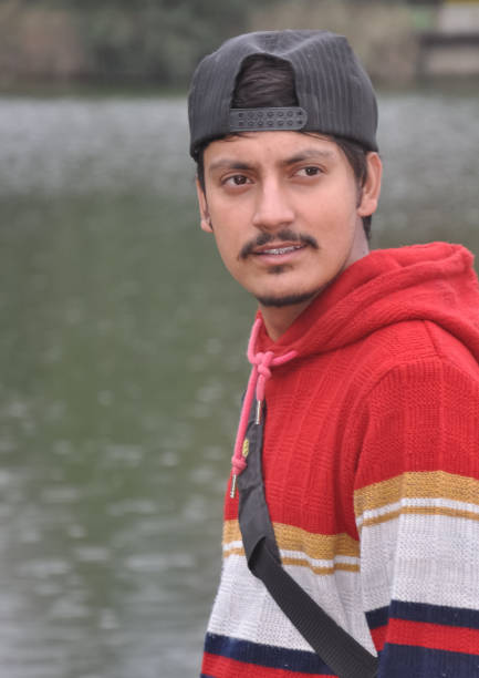istock Waist-up of a Indian young guy wearing cap backwards looking sideways while standing by the lake 1413369721