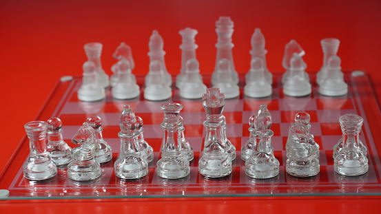 Transparent chess figures, on starting position, on reflective chess board, red tone. Strategic Chess board game