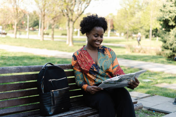 portrait of a young woman sitting at the park and reading newspaper - young adult reading newspaper the media imagens e fotografias de stock