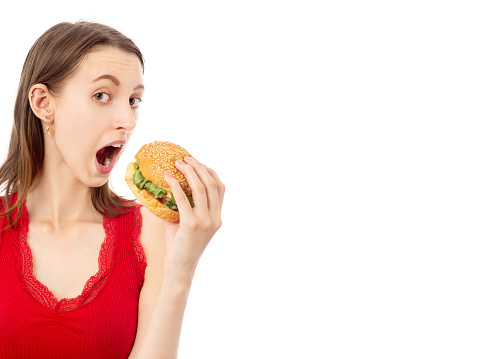 happy young woman eats hamburger on white background with copy space isolated looking at camera open mouth