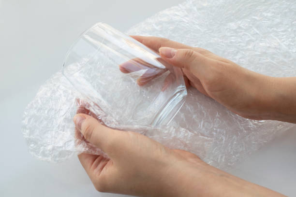 istock Woman hands packaging a glass for water with white transparent bubble pack on a white background. Material for packing fragile items for safe transportation. Close-up. 1413386103