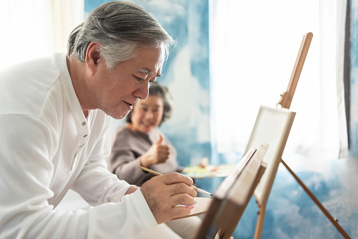 Happy Asian Senior adult Couple colouring on canvas together.