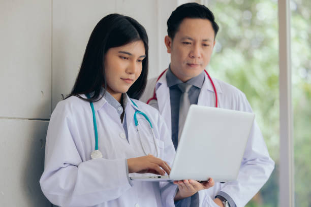 istock Asian two male female professional doctor standing using computer laptop checking patient's medical records ,Portrait doctor healthcare professionals 1413389214