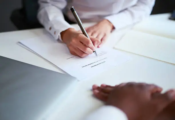 Photo of Signing a contract or agreement for an investment at a business meeting. Closeup of hands filling in a form or legal document for a financial partnership inside an office by a sales employee