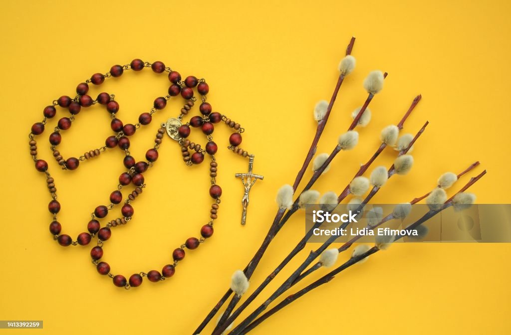 Dry willow branches and rosary wooden prayer beads crucifix on yellow background Dry willow branches and rosary wooden prayer beads crucifix on yellow background. Palm Sunday spring holiday. Holy week christian religious concept. Flatlay, lay out, top view Backgrounds Stock Photo