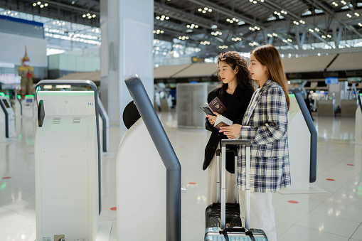 Two young businesswomen are checking in at the airport by using their mobile phones for a business trip.